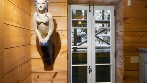 L’intérieur d’un chalet en bois, avec une sculpture en bois, une porte dotée de panneaux de verre et une vue sur un paysage enneigé.