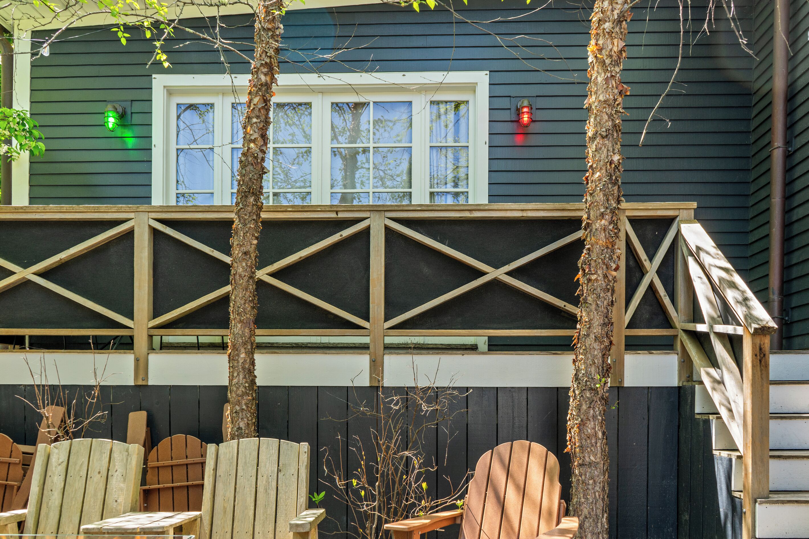 A building with a dark exterior, a white-framed window, and a wooden deck with chairs.