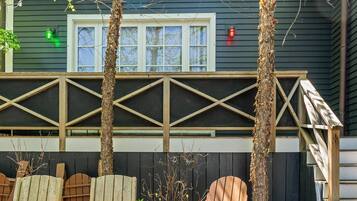 A building with a dark exterior, a white-framed window, and a wooden deck with chairs.