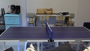 A ping pong table with GoGames branding, a coffee machine, and a painting of a beach scene on the wall. - Welcome to the Pool House Retreat! (Jonesboro)