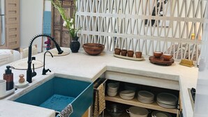 A kitchen with a blue sink, hanging wicker lamps, a white partition, and a variety of kitchenware.