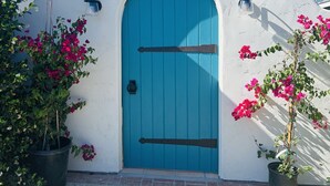 A house with a blue door, white walls, and a small garden with pink flowers.
