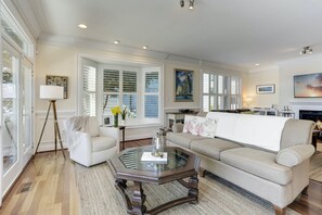 A spacious living room with a large sofa, a glass coffee table, and a fireplace. - This thoughtfully styled home overlooks the Bay and is perfect for your Annapolis escape. (Annapolis)