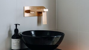 Un baño con un lavabo negro, una botella de jabón de manos Glow Lab y un grifo dorado.