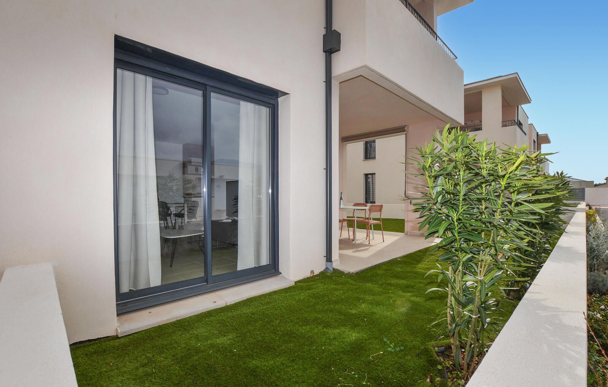 Eine moderne Wohnung mit einer Schiebetür zum Garten, einer kleinen Terrasse mit Tisch und Stühlen und einem gepflegten Rasen.