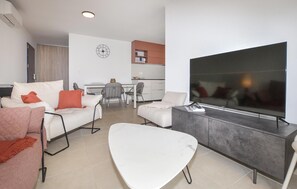 A modern living room with a flat-screen TV, a dining area with chairs, and a kitchen in the background. - 2 bedroom stunning apartment in Folelli (Folelli)