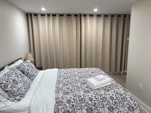A neatly made bed with a floral bedspread and pillows, a lamp on a bedside table, and a window with vertical blinds. - Lovely House walking to Niagara Falls in Canada (Niagara Falls)