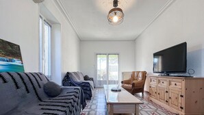 A living room with a sofa, a coffee table, a TV on a cabinet, and a patterned floor. - Maison av. piscine proche Uzès (Saint Laurent la verne)