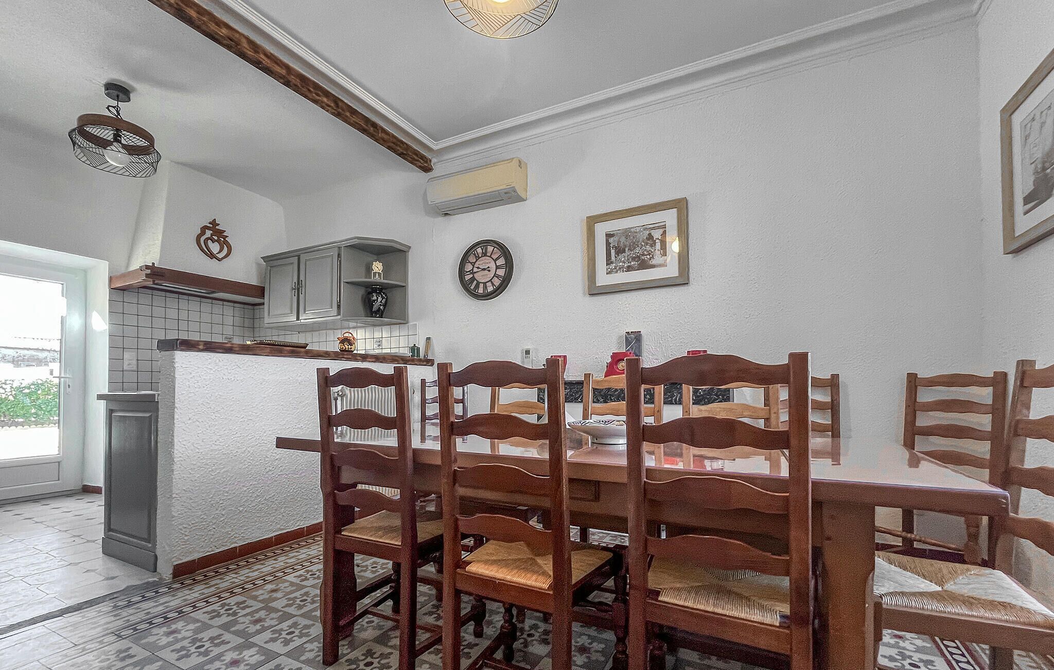 Zona pranzo con tavolo e sedie in legno, cucina con pensili, una sveglia e un quadro appeso al muro.