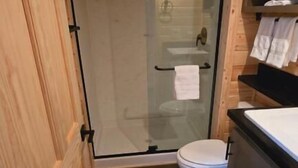 A small bathroom with a glass shower door, a toilet, and wooden cabinetry. - Luxury Cabin with Mountain View 3B (Williams)