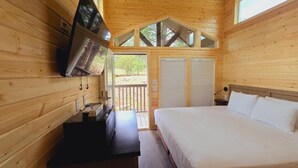 A wooden cabin room with a bed, a TV mounted on the wall, and a sliding door leading outside. - Luxury Cabin with Mountain View 3B (Williams)