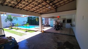 A covered outdoor area with a pool, lounge chairs, and a dining table. - Cozy house with pool, air conditioning, barbecue, and garage. (Armação dos Búzios)
