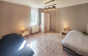 Ein Schlafzimmer mit zwei Betten, einem Fenster mit Vorhängen, einem Heizkörper und einem Kleiderschrank.