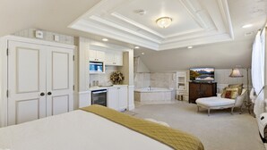 Een slaapkamer met een groot bed, een badkamer met een badkuip, en een televisie.