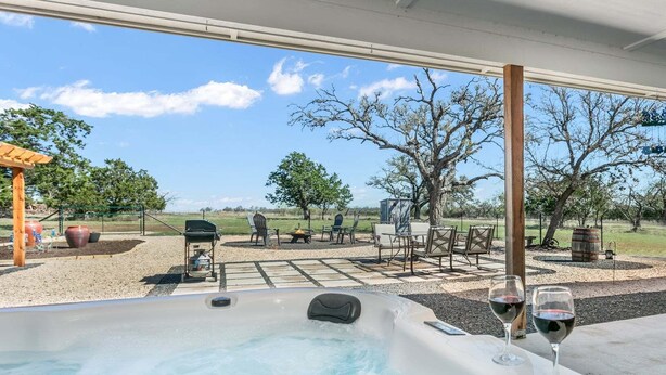 Ett bubbelbad med två glas vin, utomhusmöbler och utsikt över ett lantligt landskap.