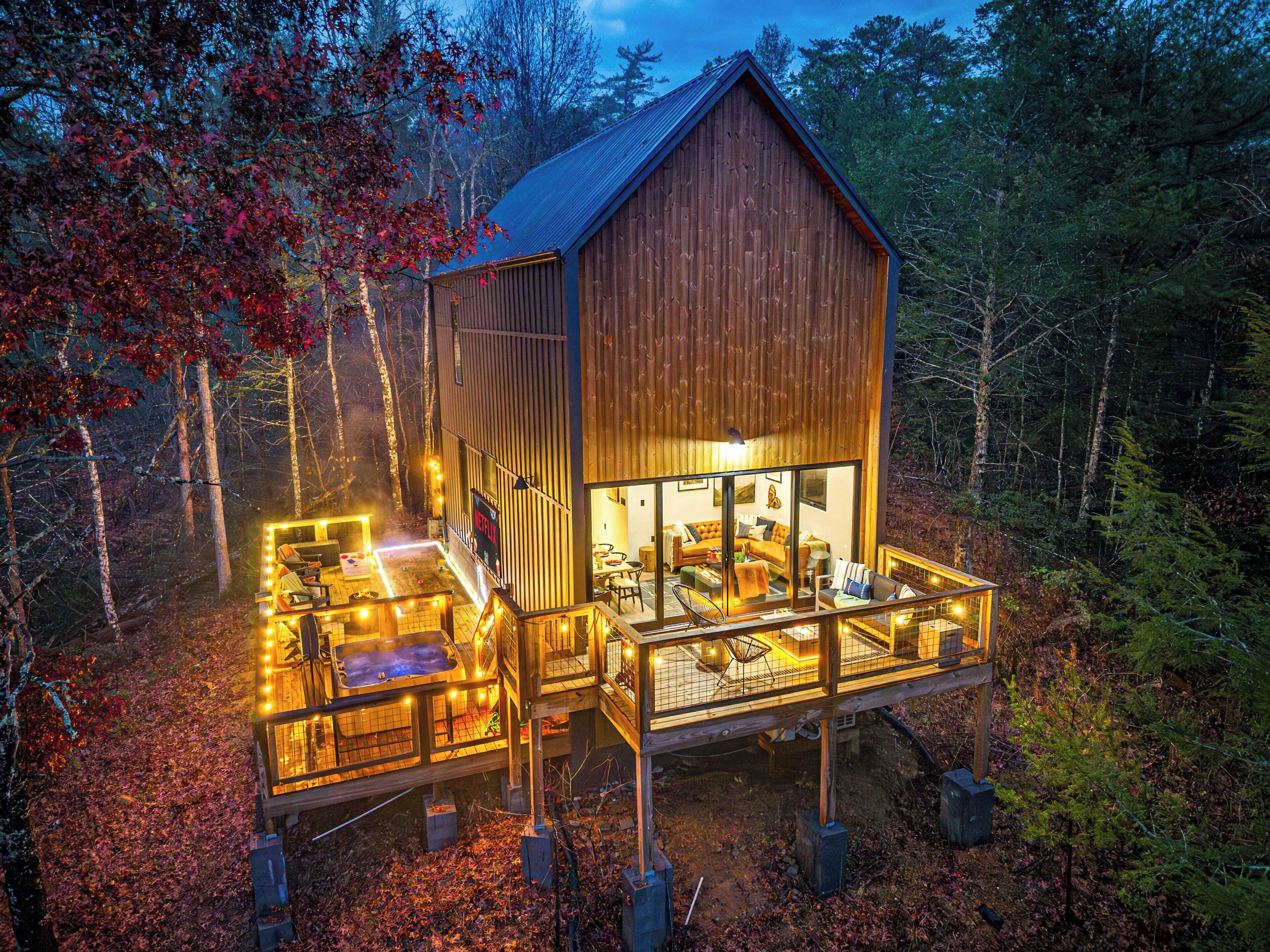 A wooden cabin with a deck, a hot tub, and a large window overlooking the forest.