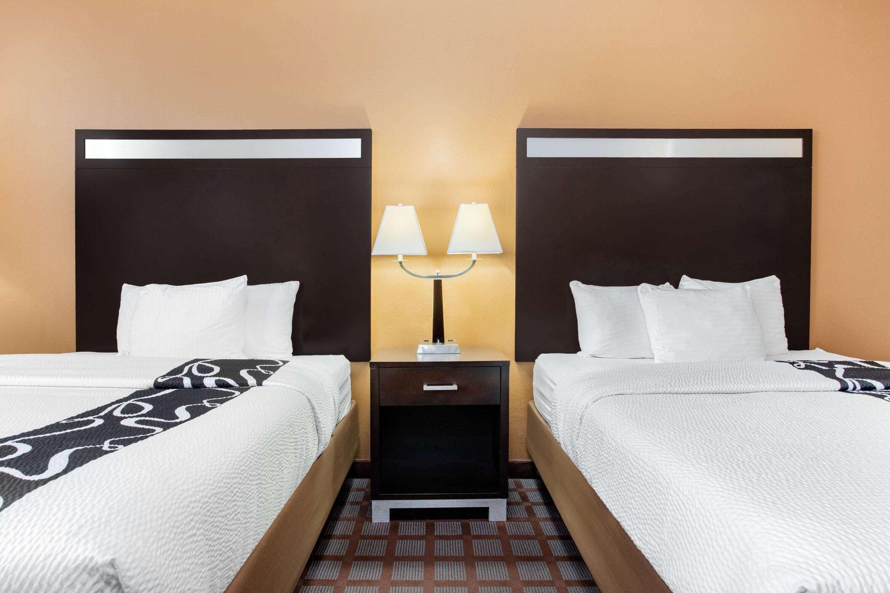 A hotel room with two beds, a nightstand with a lamp, and a patterned carpet.