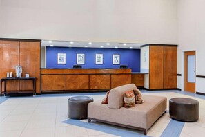 Un área de recepción con sofá, reposapiés y escritorio con obras de arte enmarcadas.