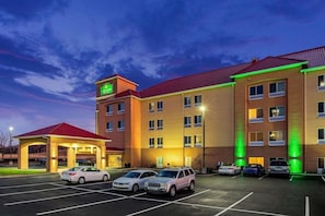 A hotel with a red roof, multiple floors, and a parking lot with several cars. - La Quinta Inn & Suites Indianapolis Airport West (Plainfield)
