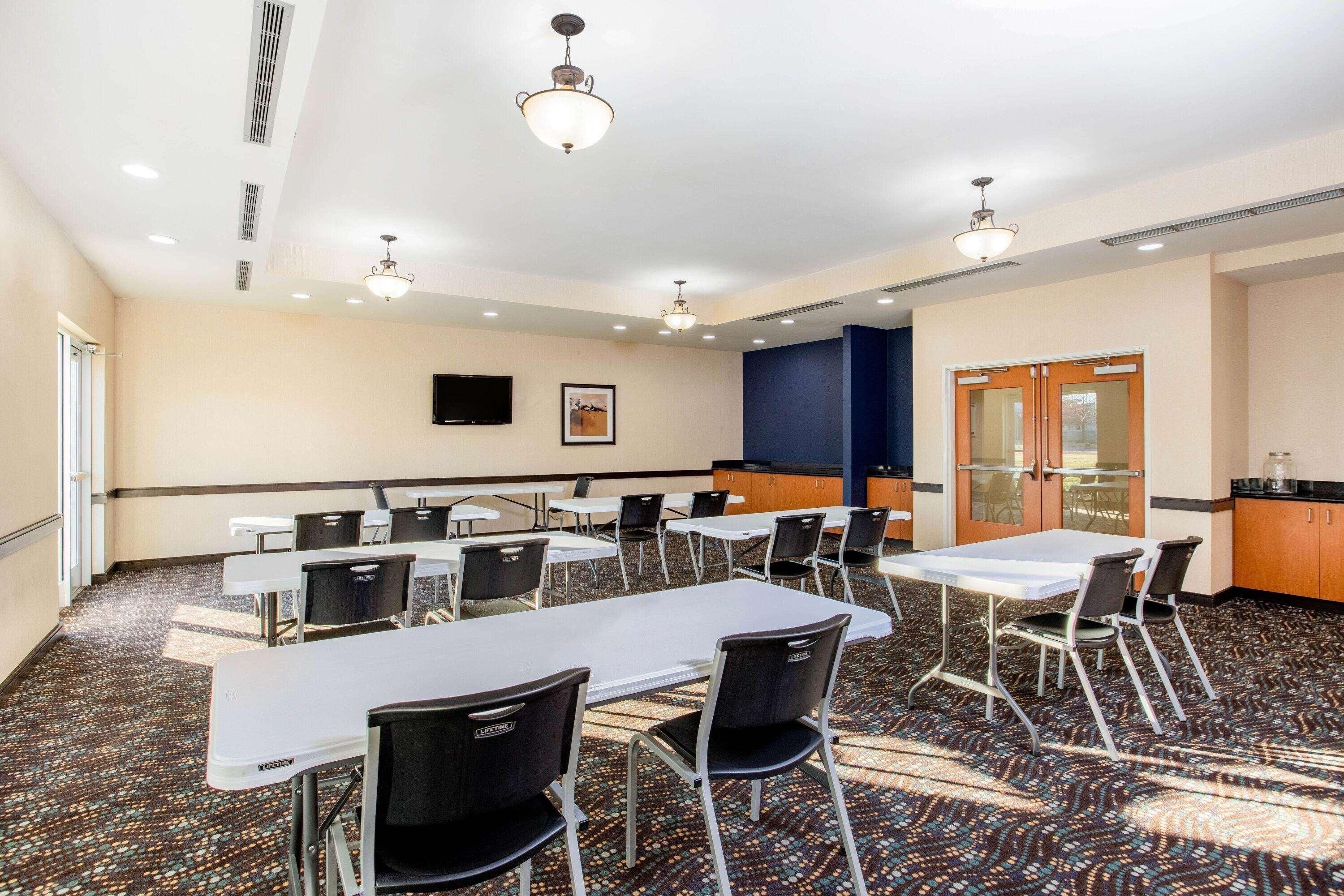 A conference room with tables, chairs, a television, and a kitchen area.