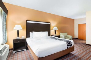 A hotel room with a large bed, two bedside tables with lamps, a chair, a heater, and a wardrobe. - La Quinta Inn & Suites Indianapolis Airport West (Plainfield)