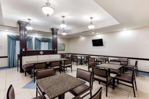 Un comedor de hotel con varias mesas y cabinas, ventiladores de techo y un televisor de pantalla plana en la pared.