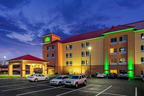 A hotel with a red roof, multiple floors, and a parking lot with several cars. - La Quinta Inn & Suites Indianapolis Airport West (Plainfield)