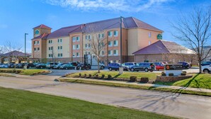 A hotel with a central courtyard, multiple parking spaces, and a clear sky. - La Quinta Inn & Suites Indianapolis Airport West (Plainfield)