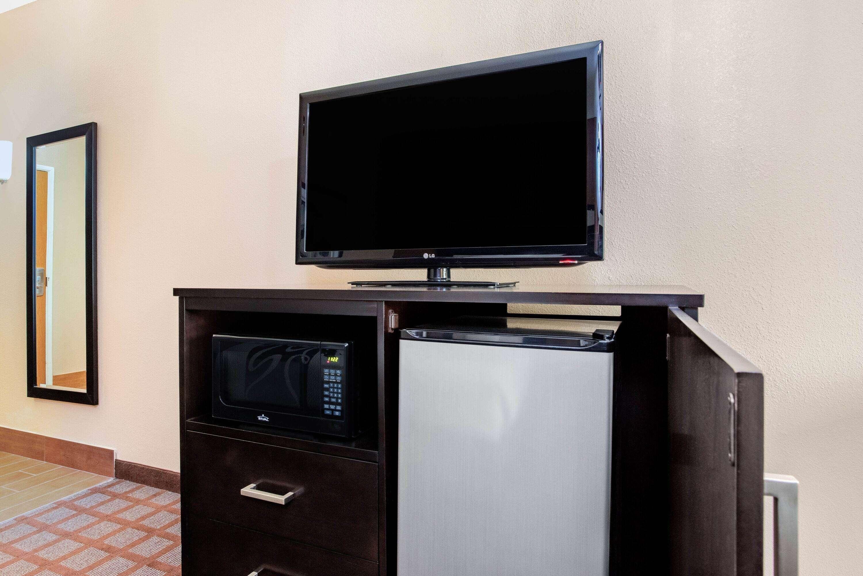 Habitación de hotel con televisión de pantalla plana montada en un mueble de madera oscura, microondas y refrigerador.