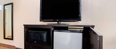 Habitación de hotel con televisión de pantalla plana montada en un mueble de madera oscura, microondas y refrigerador.