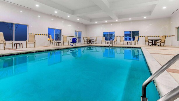 A swimming pool with chairs and tables, large windows, and a tiled floor. - La Quinta Inn & Suites Indianapolis Airport West (Plainfield)