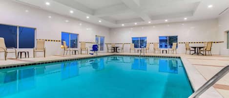 A swimming pool with chairs and tables, large windows, and a tiled floor.
