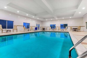 A swimming pool with chairs and tables, large windows, and a tiled floor. - La Quinta Inn & Suites Indianapolis Airport West (Plainfield)