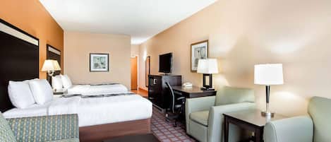 A hotel room with a bed, two chairs, a desk, a TV, and a lamp.