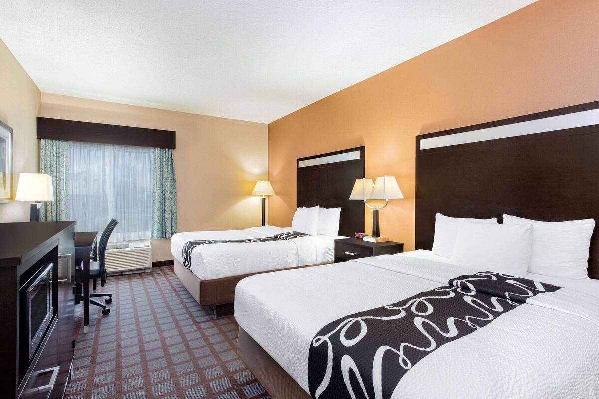 A hotel room with two beds, a desk, a chair, and a window with curtains.