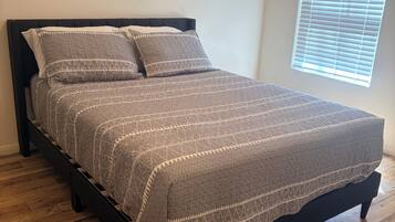 A bed with a patterned bedspread, a black headboard, and a window with blinds.