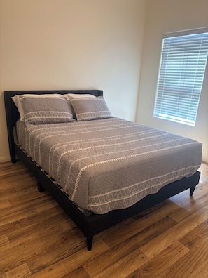 A bed with a patterned bedspread, a black headboard, and a window with blinds.