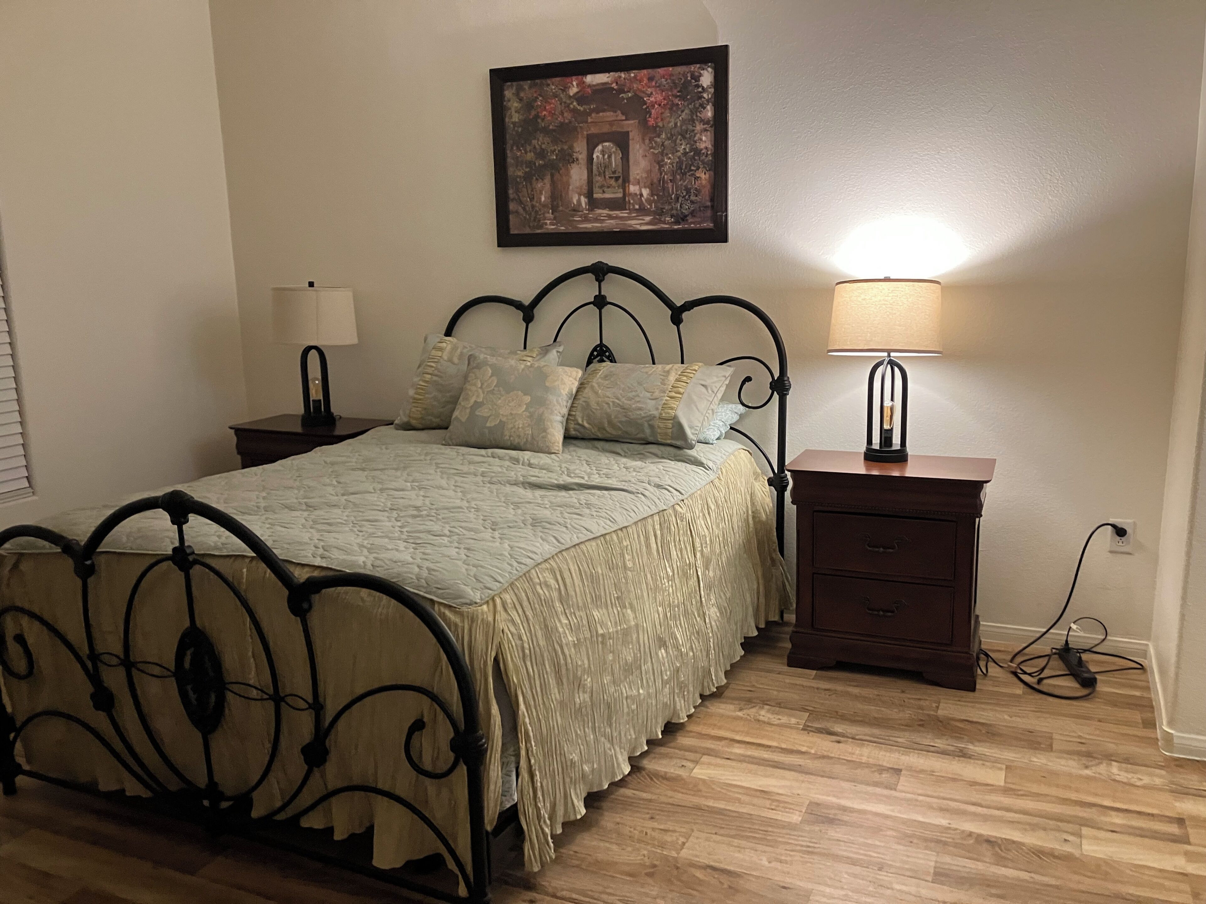 Ein Schlafzimmer mit einem Bett, Nachttischen, einer Lampe, einem Gemälde und Holzboden.