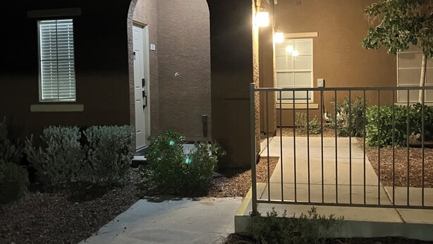 Un edificio residencial con un acceso cubierto, una puerta a la vista y un pequeño jardín con plantas.