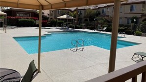 Una piscina con zona sombreada, sillas de descanso y un área de estar cubierta.