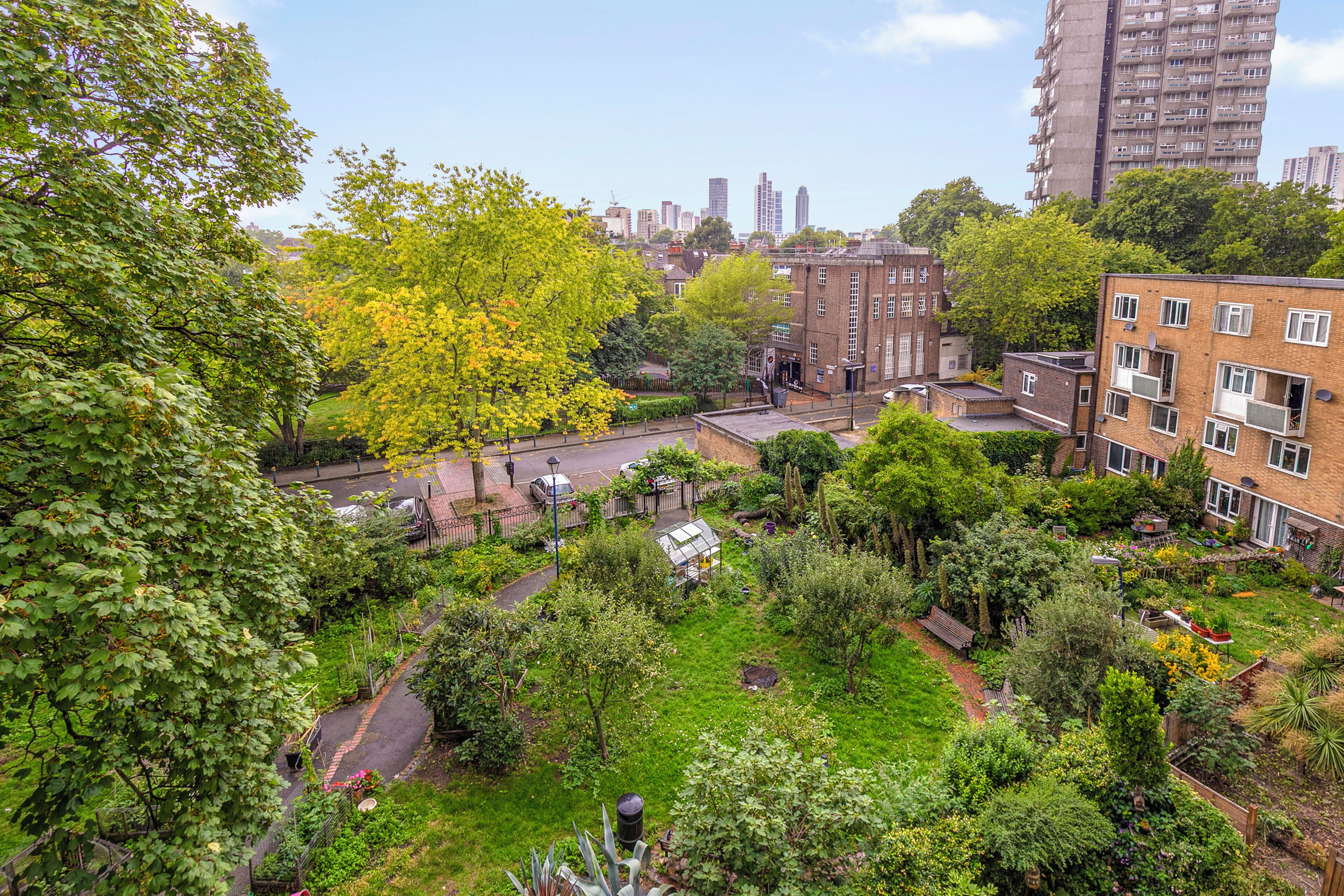 A residential area with a garden, a brick building, and a tall apartment building in the background.