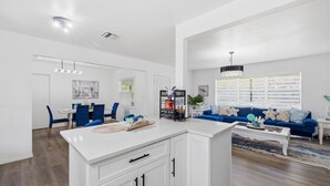 A spacious living area with a dining table, blue chairs, a blue sofa, and a white kitchen island. - Clearwater Paradise/Hot Tub & Backyard Bliss/Near Beach+Hotspots (Clearwater)