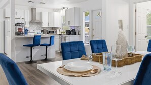 A modern kitchen with white cabinets, a central island, blue bar stools, and a dining table set with plates and glasses. - Clearwater Paradise/Hot Tub & Backyard Bliss/Near Beach+Hotspots (Clearwater)