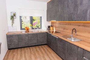 Une cuisine moderne avec un plan de travail en bois, des meubles gris, un évier et une fenêtre agrémentée de plantes.
