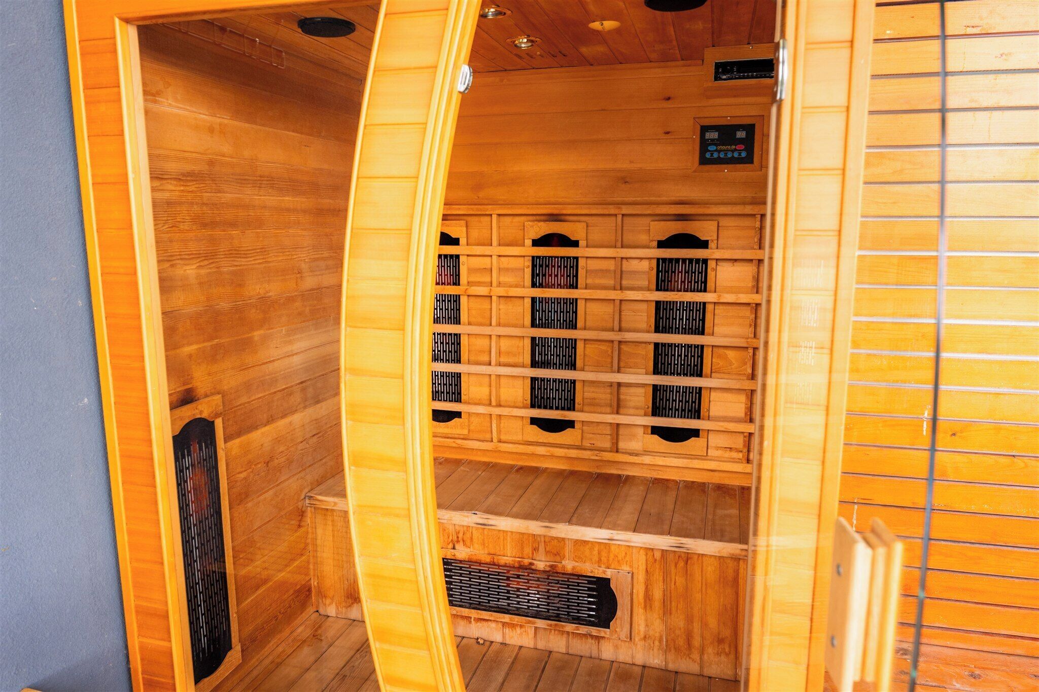 A wooden sauna with a sloped ceiling, a ventilation system, and a control panel.