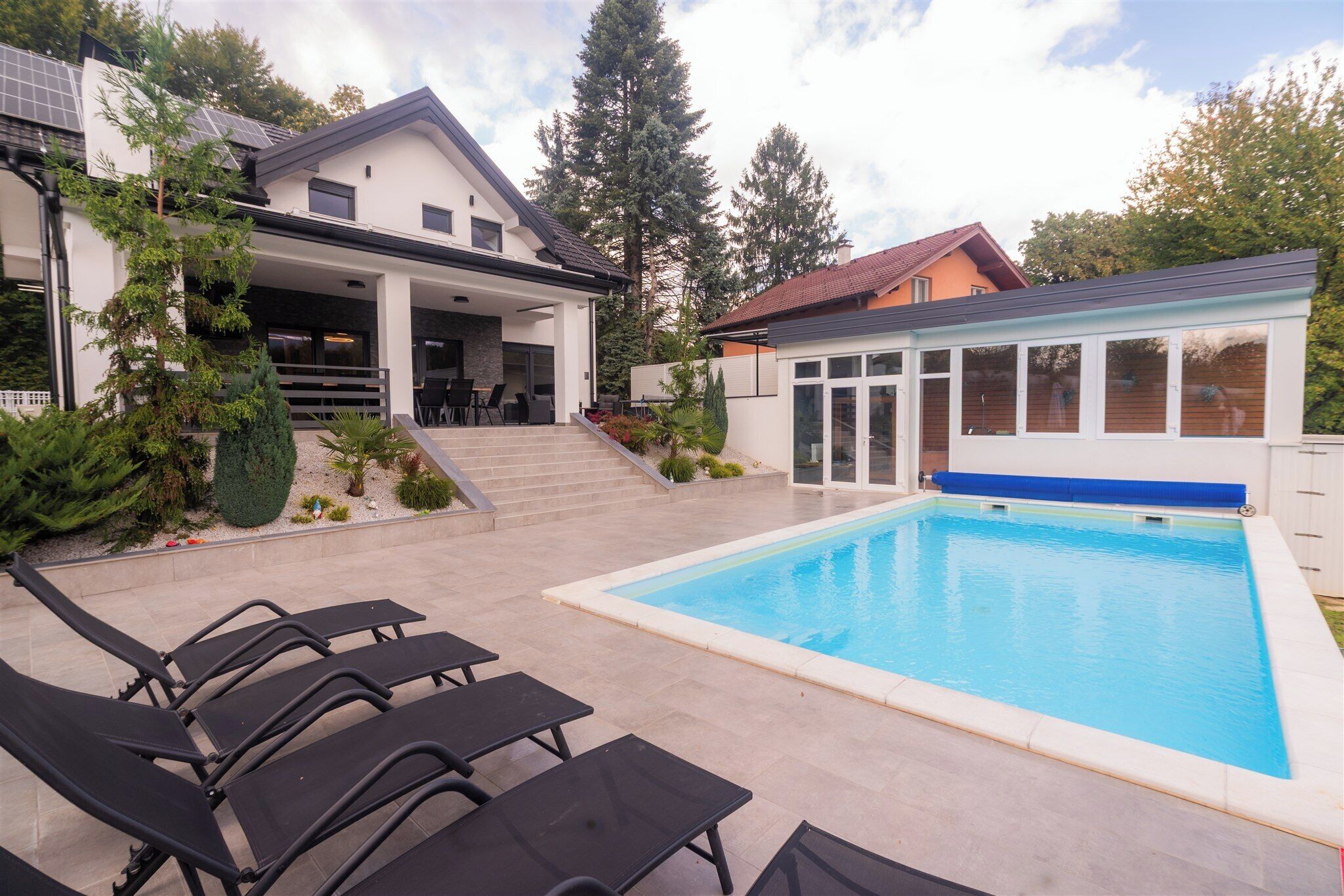 A modern house with a swimming pool, outdoor seating, and a covered patio.