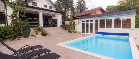 A modern house with a swimming pool, outdoor seating, and a covered patio.