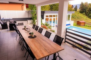 Une table à manger en bois avec des chaises, une piscine et une vue sur une maison et des collines.