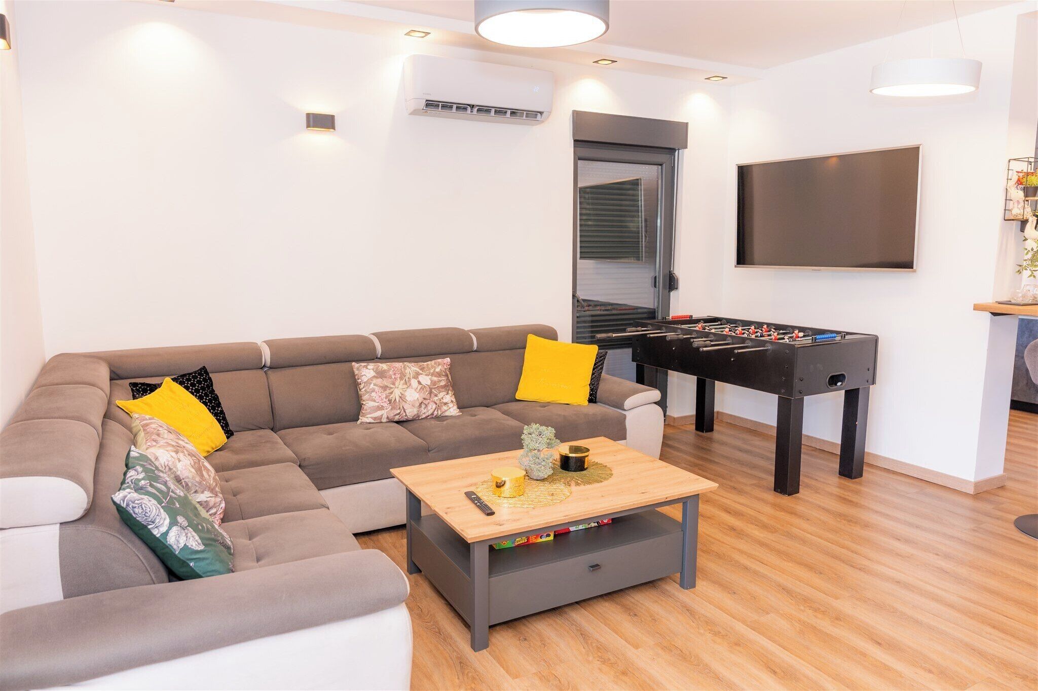 Ein Wohnzimmer mit einer Couch, Couchtisch, Kicker und einem Flachbildfernseher.
