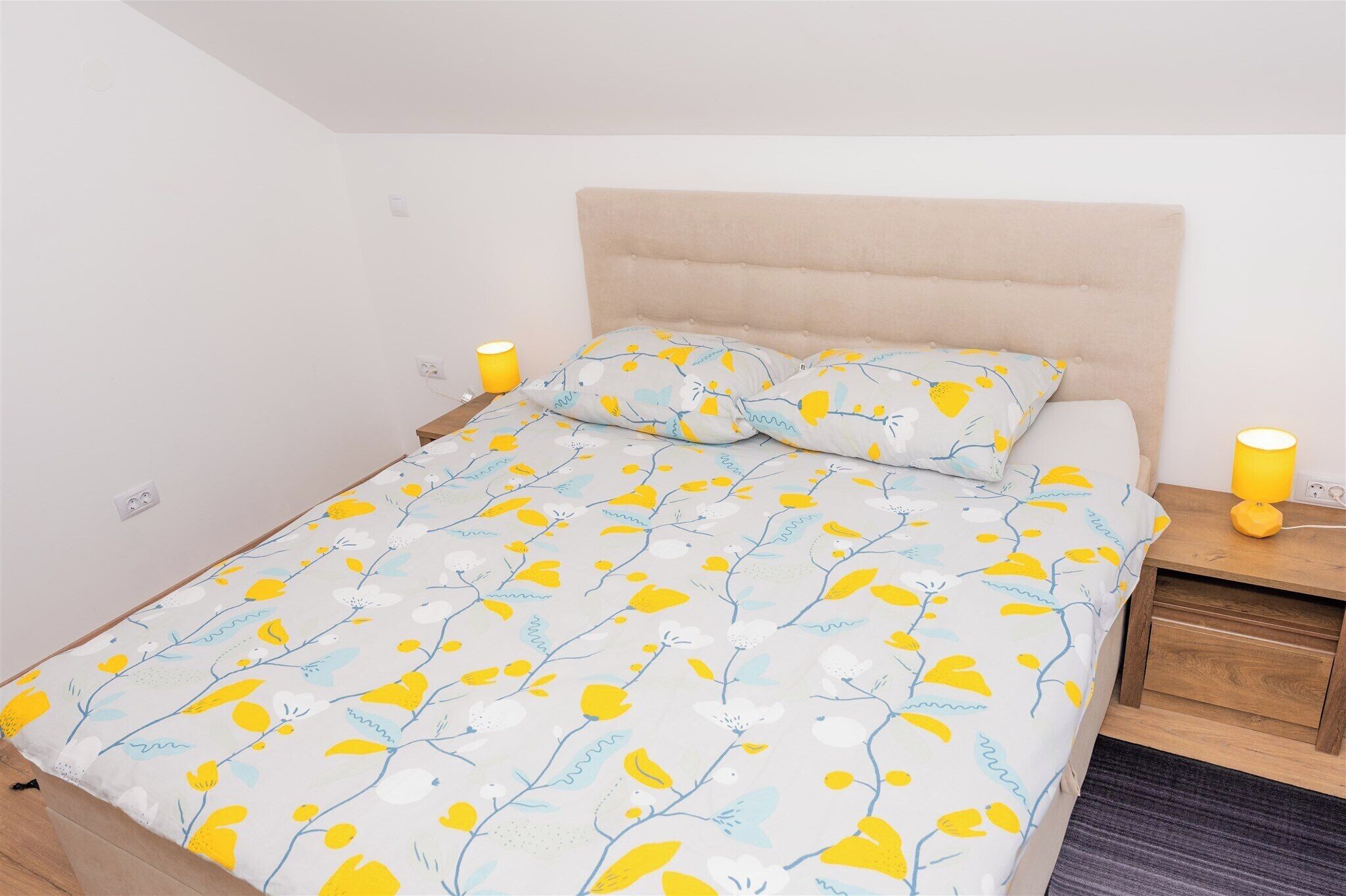 A bed with a floral bedspread, two bedside lamps, a wooden nightstand, and a headboard.